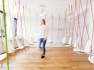 Der Kreativraum der Wohngemeinschaft zeigt einen großen Raum mit vielen schwebenden Stühlen. Die Stühle sind mit Seilen an der Decke verbunden.
