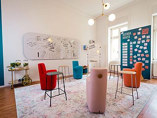 Ein Workshop-Raum, der mit bunten Möbeln, Whiteboards und Tafeln eingerichtet ist.